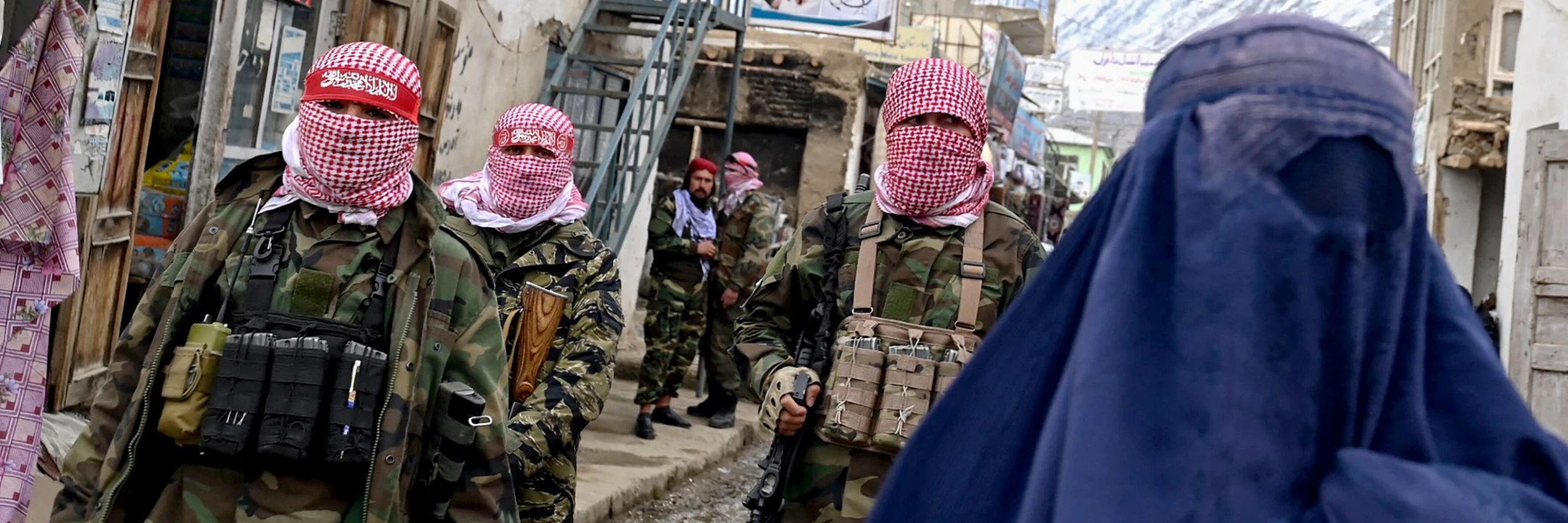 Taliban-Sicherheitskräfte stehen Wache, während eine afghanische Frau auf einem Markt entlanggeht © AFP / Wakil Kohsar
