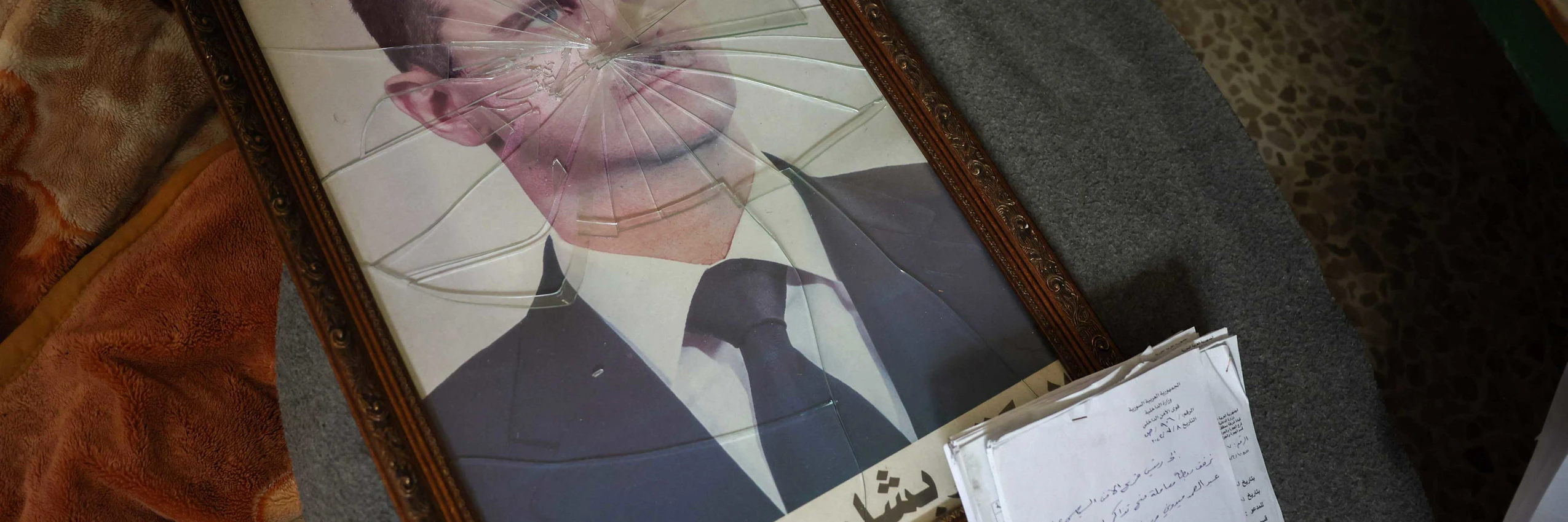 Ein Portrait des gestürzten syrischen Machthabers Bashar al-Assad hinter zerbrochenem Glas © OMAR HAJ KADOUR / AFP / picturedesk.com