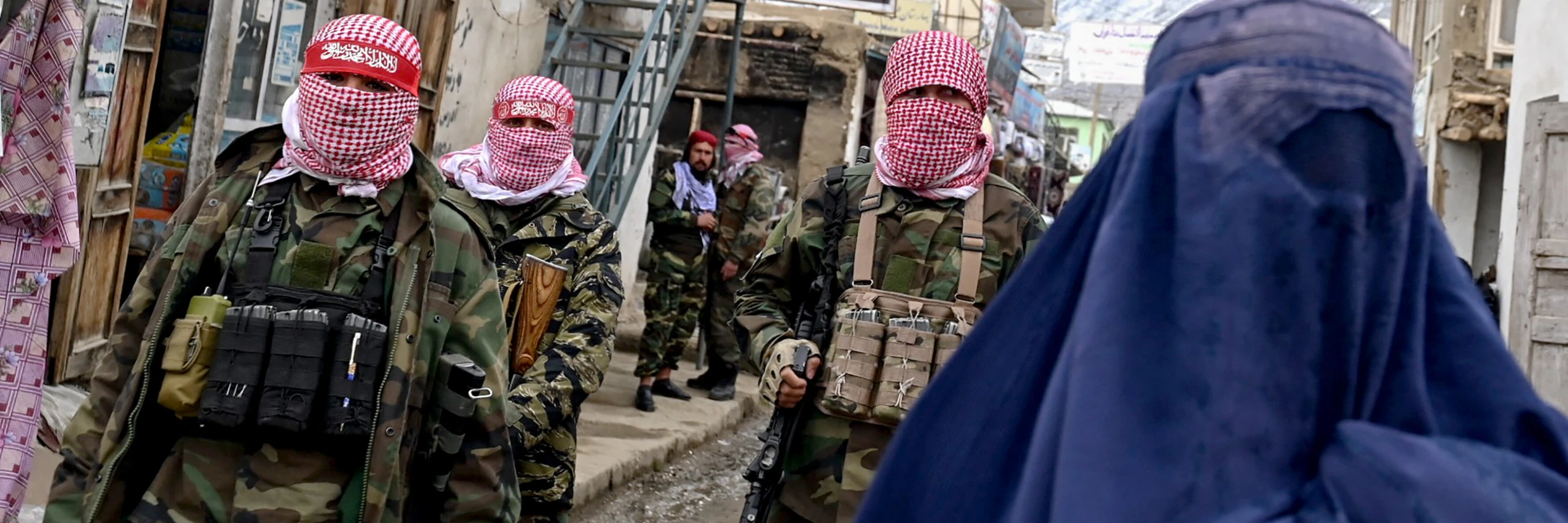 Taliban stehen Wache, während eine afghanische Frau in Burka eine Straße entlanggeht. © WAKIL KOHSAR