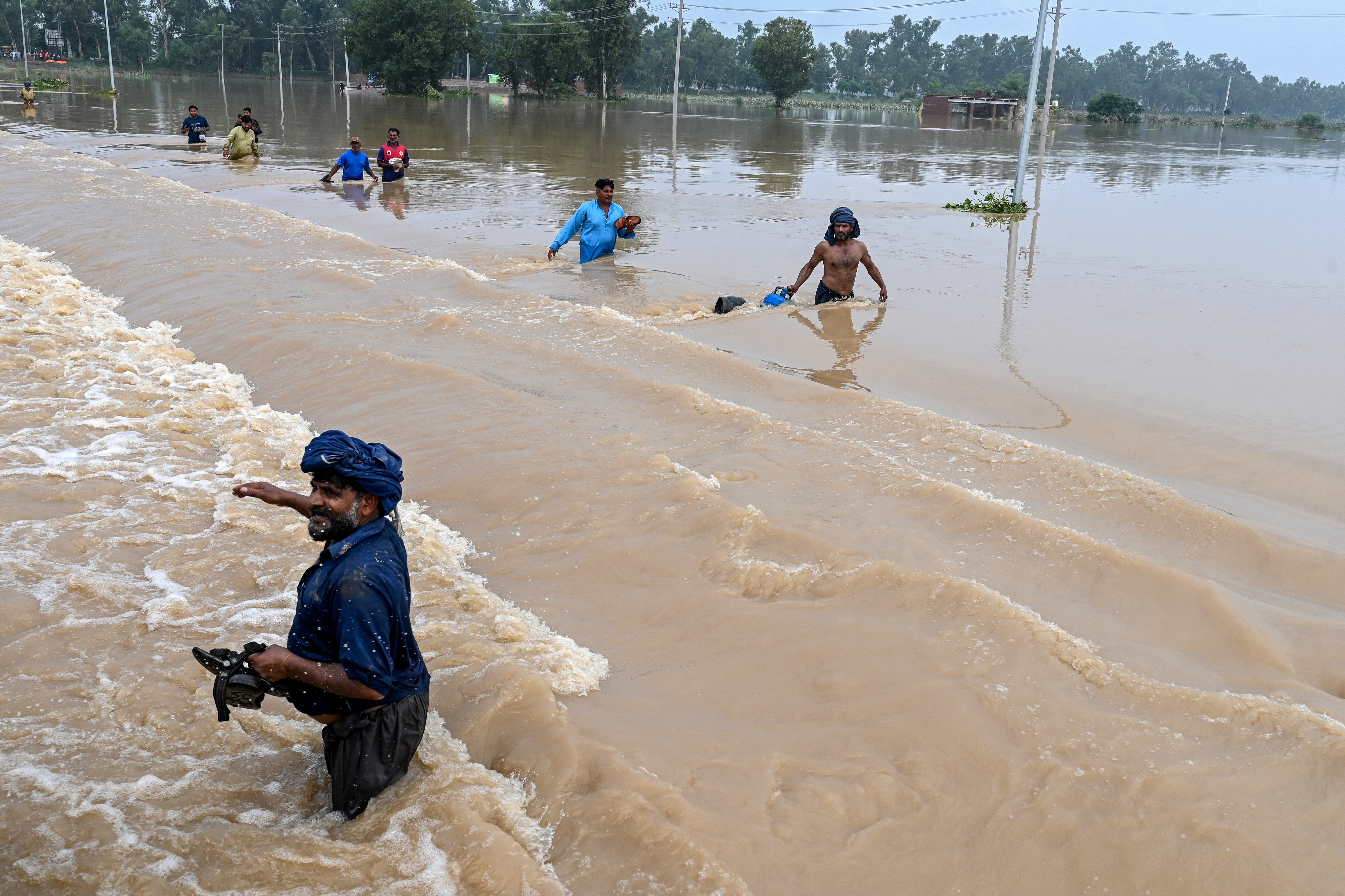 Anwohner*innen waten durch überflutete Straßen in Kartarpur, Pakistan, 28. August 2025. Extreme Monsunfluten zwangen die Behörden zur kontrollierten Sprengung eines Dammdeiches, um die Struktur zu retten. © ARIF ALI/AFP via Getty Images