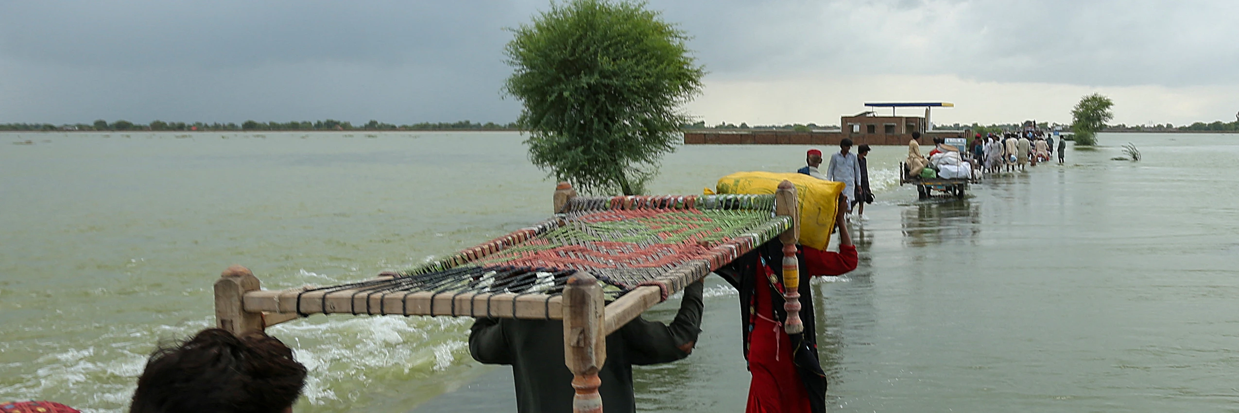 Menschen verlassen ihre Dörfer und tragen ihre Habseligkeiten durch überschwemmte Gebiete, um höher gelegene Orte im südlichen Punjab zu erreichen, 25. August 2022. © Getty / Shahid Saeed Mirza