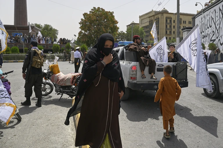 Eine Frau geht am 15. August 2025, in Kabul, Afghanistan, zügig durch eine Menschenmenge aus Taliban-Kämpfern und -Anhängern, die gerade den vierten Jahrestag des US-Abzugs und den Beginn der Taliban-Herrschaft feiern. @ AP Photo/Nava Jamshidi