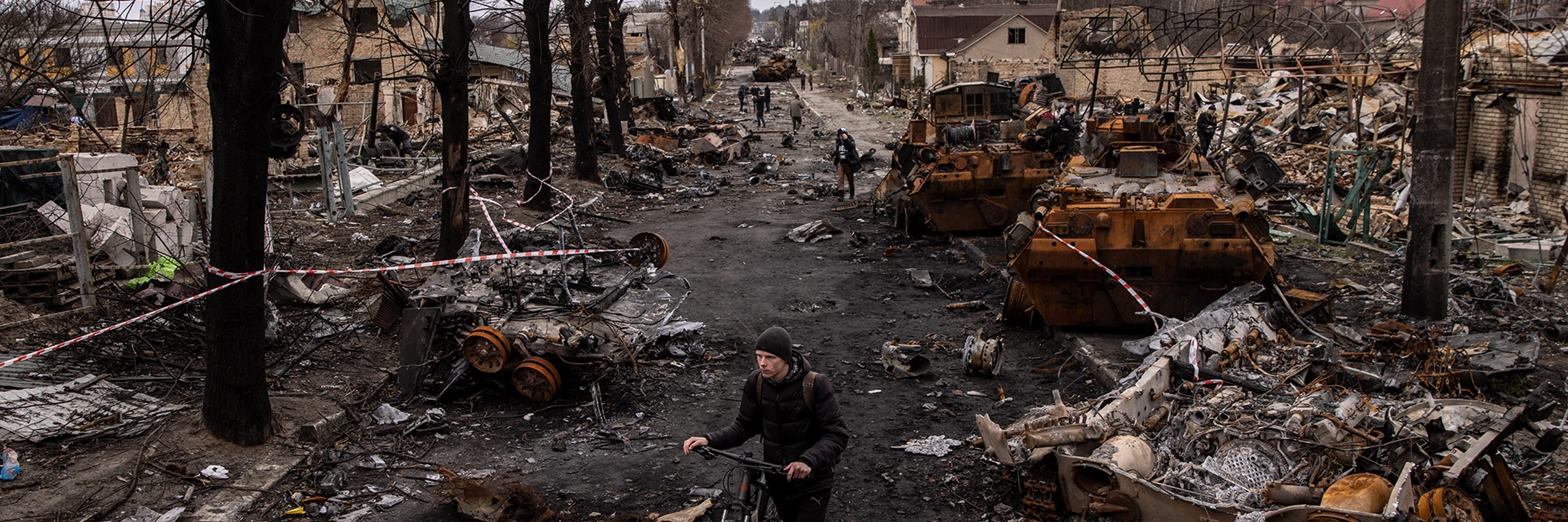Butscha, Ukraine, am 06. April 2022: Ein Mann schiebt sein Fahrrad durch Trümmer und zerstörte russische Militärfahrzeuge auf einer Straße. © Chris McGrath/Getty Images