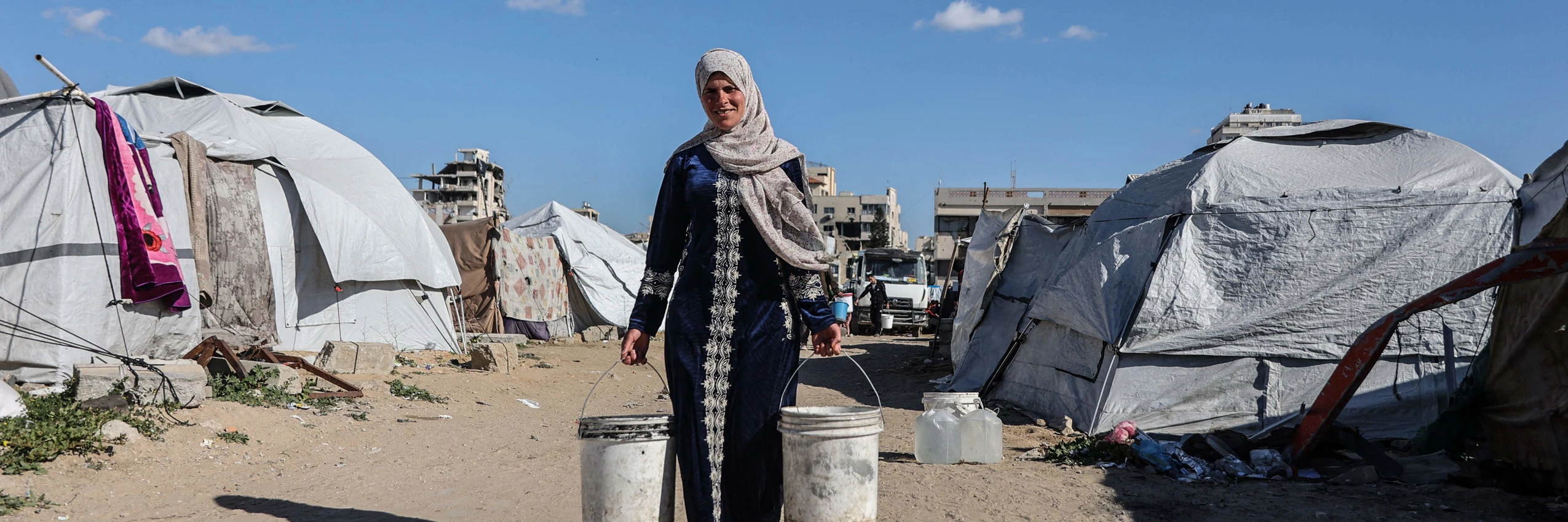 Eine vertriebene palästinensische Frau trägt in Gaza-Stadt Behälter mit Trinkwasser © APA-Images / AFP / OMAR AL-QATTAA