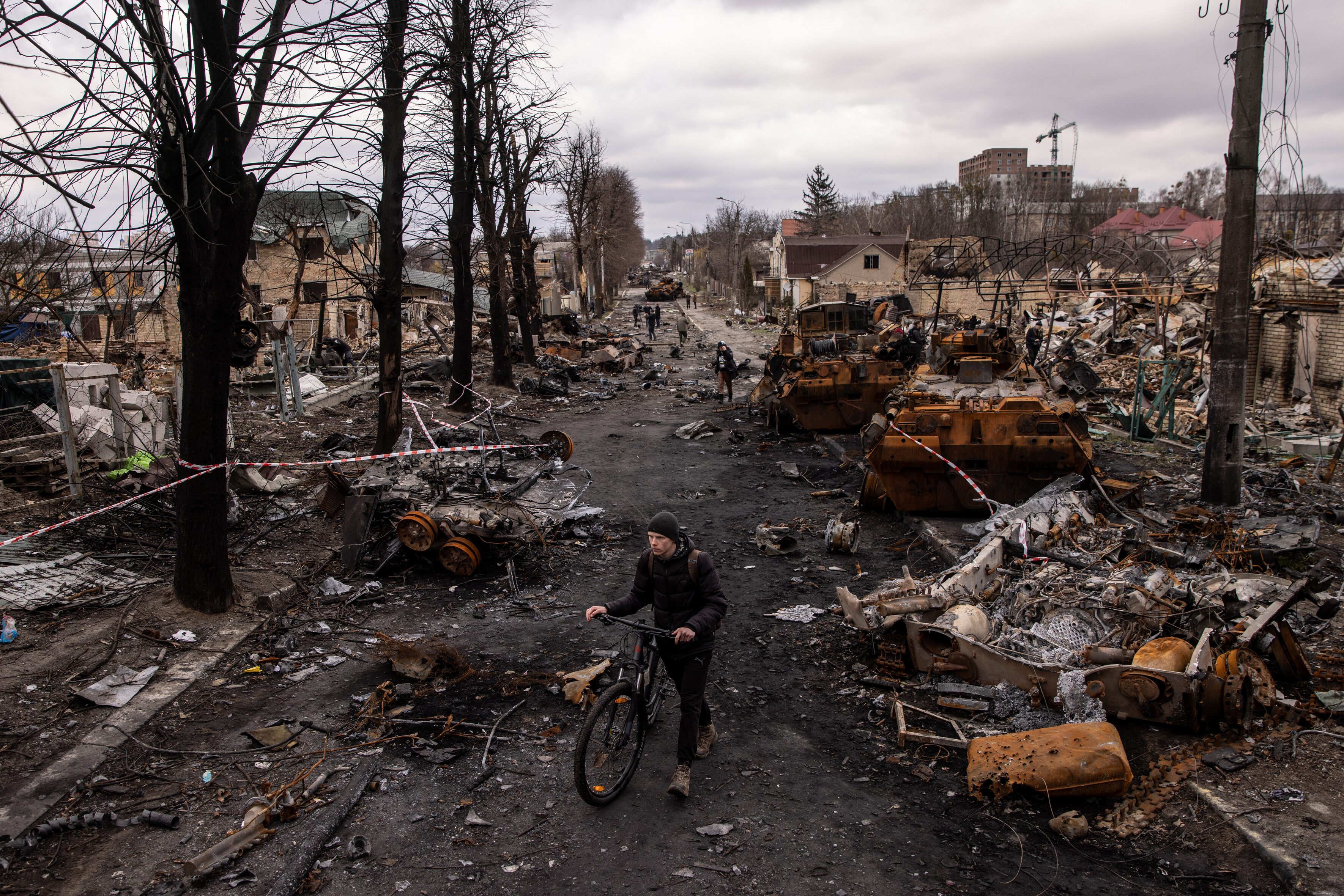 Ein Mann schiebt sein Fahrrad durch Trümmer und zerstörte Militärfahrzeuge auf einer Straße in Bucha, Ukraine. © Chris McGrath