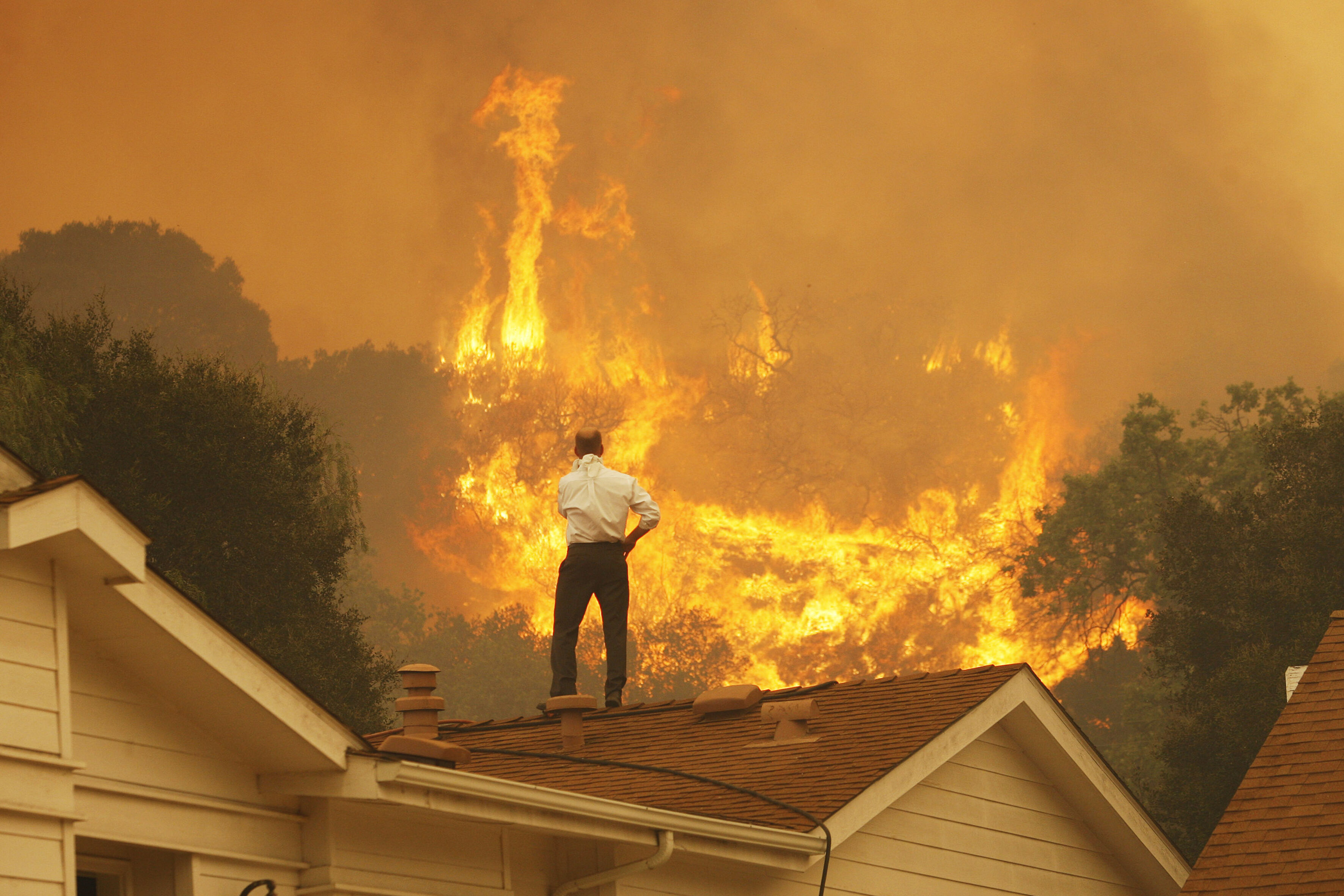 Ein Mann auf einem Dach blickt auf die nahenden Flammen eines Waldbrandes in Kalifornien – ein Bild der eskalierenden Klimakrise. © David McNew/Getty Images