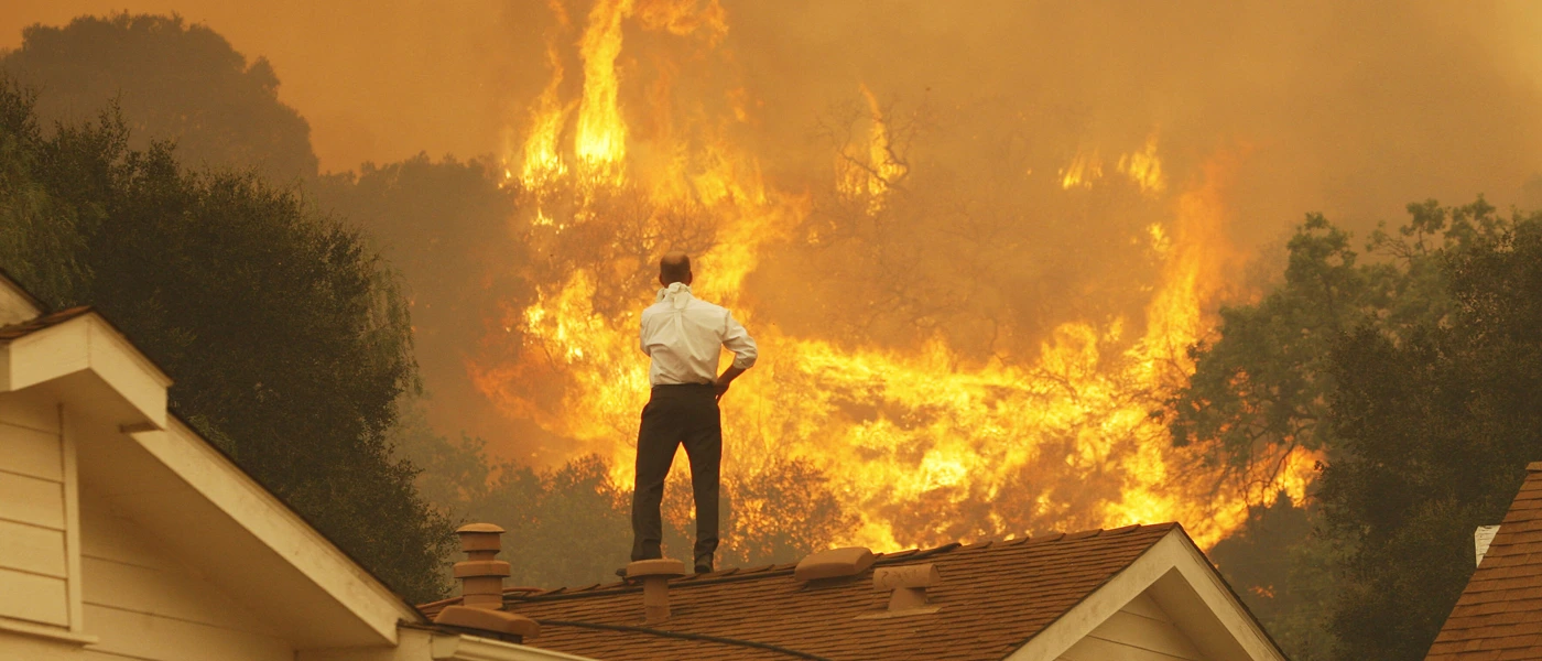 Ein Mann auf einem Dach blickt auf die nahenden Flammen eines Waldbrandes in Kalifornien – ein Bild der eskalierenden Klimakrise. © David McNew/Getty Images